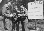 Three British soldiers hold a conversation beside a sign which announces that entry into the Bergen-Belsen concentration camp is prohibited due to a typhus epidemic.
