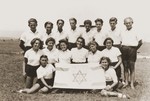 Members of the Zionist youth group Hanoar Hatzioni pose with their movement's flag at a refugee camp for the Kladovo transport.