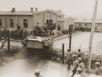 Allied POWs, imprisoned in a camp near Hammelburg, cheer as an American tank crashes through the barbed wire enclosure of the prison camp.