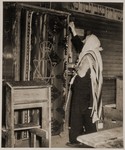 A man wearing a prayer shawl and phylacteries stands in front of the Torah ark at a displaced persons camp in Sankt Marien, Austria.