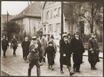 A small group of Jews, who have been rounded-up for arrest after Kristallnacht, is escorted down a street by German police, SA and SS members.