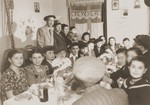 Motel (Mordechai) Appelbaum (sitting beneath a sign) celebrates his Bar Mitzvah with family and friends in the Gabersee displaced persons camp.