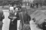 A Polish woman holding her child converses with her soldier husband, who supervises a group of civilians digging an anti-tank trench along a street in Warsaw to slow the advance of the German army.