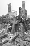 Stacks of crucifixes lie against the brick wall of a destroyed church or cemetery structure in Warsaw.