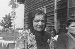 Portrait of an elderly, Jewish DP woman, who is seated outside on a bench among other women who are knitting, at a displaced persons camp in Austria.