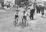 Two Jewish children ride tricycles along a street in Rymanow, Poland.
