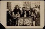 A group of young Jewish men and women sit around a table during a Saturday night party in Eisiskes.