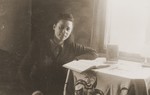 Zoia Bershtanski sits in front of an open book at a table in her room in the Kovno ghetto.