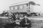 Three Romani brothers sit outside in front of a caravan reading a newspaper.