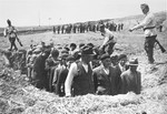 Romanian soldiers direct men into rows in a ditch, presumably before their mock execution.