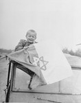 Five year-old Briner Odon sits on top of an American jeep holding a Star of David flag just prior to his departure from Buchenwald to France.