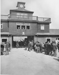Visiting radio commentators, on an official tour of the war front, wait at the entrance to newly liberated Buchenwald concentration camp.