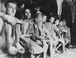 Wounded and sick survivors, Russians, Poles, and Jews, sitting on a bench inside a barracks in Buchenwald concentration camp.