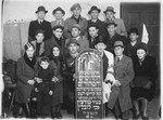 Jewish survivors from Turobin pose with a memorial plaque commemorating the victims of Nazism from their community.