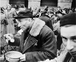 A man who has just arrived in Theresienstadt with a transport of Dutch Jews eats from a bowl in the main courtyard of the ghetto.