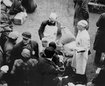View from above of a prisoner wearing a cook's uniform doling out food in the ghetto courtyard to prisoners who have just arrived in Theresienstadt with a transport of Dutch Jews.