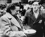 A woman who has just arrived in Theresienstadt with a transport of Dutch Jews holds a bowl of soup in the main courtyard of the ghetto.