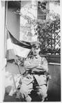 Werner Cohn, a German-Jewish soldier, sits outside his home in his army uniform next to a German flag.