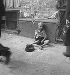 A small boy begs on the sidewalk in the Warsaw ghetto.