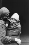 A destitute mother holds a child swaddled in a ragged blanket on a street in the Warsaw ghetto.