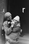 A destitute mother holds a child swaddled in a ragged blanket on a street in the Warsaw ghetto.