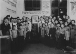 Members of the Betar revisionist Zionist youth movement pose alongside a memorial display featuring a portrait of Joseph Trumpeldor and a Hebrew plaque that reads, "There is nothing better than to die for our land".