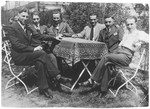 A group of young Jewish men wearing suits and ties sits outside around a table.