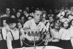 Szlomo Waks, the prize singer of the Children's Center School, lights a Hannukah menorah during a holiday celebration in the Zeilsheim displaced persons' camp.