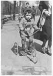 A young Jewish boy rides his tricycle down a street in Krakow.