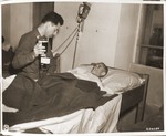 Captain Richard Berman of Philadelphia administers plasma to Roszi Frank, an emaciated survivor of a death march, in an American field hospital in Volary.