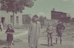 A woman and children all of whom are wearing yellow stars stand on a street corner of the Lodz ghetto.