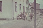 A group of boys, one with a scooter, stand on a street corner in the Lodz ghetto.