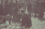 A man sits on the ground next to some used wares he is selling in the outdoor market of the Lodz ghetto.
