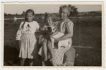 A young Jewish girl in hiding sits on the lap of her rescuer in a farm in eastern Poland while an older Jewish girl in hiding stands next to them.