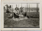 A couple with their young child sits on the grass near the barbed wire fence of the Gurs internment camp.