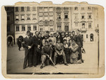 A group of friends, many of whom are wearing university caps, pose for a group portrait on a street in Warsaw.