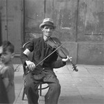 A man on the street plays the violin in the hope of receiving food or money.