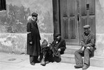 Three Jewish men sit outside the entrance to a building in the Warsaw ghetto.