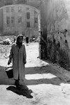 A Jewish woman carries a pail along a street in the Warsaw ghetto.