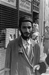 Portrait of a young Jewish man in front of a gated shop in the Warsaw ghetto.