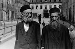 Two bearded, religious Jews walk across a courtyard in the Warsaw ghetto.
