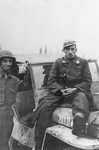 A captured German guard sits on top of a jeep, while an American soldier Julius Bernstein stands on his right.
