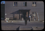 Several men enter a building at a displaced person's camp in Berlin, as young children play along the road.