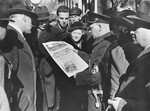 Viennese civilians crowd around a uniformed Nazi holding the morning edition of the Wiener Montagblatt newspaper announcing Hitler's arrival in Vienna.