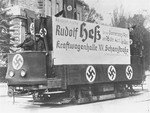 A streetcar adorned with swastikas and a large sign advertising a speech to be delivered by Reichsminister Rudoph Hess on April 7, 1938, in support of the Anschluss.