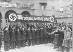 The Vienna Boys' Choir, assembled under a banner that reads, "We sing for Adolf Hitler!" salute Adolf Hitler and his entourage during his first official visit to Vienna after the Anschluss.
