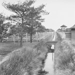 View of a section of the barbed-wire fence, moat and line of guard towers that surround the Vught transit camp.