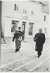 Two Jewish men, carrying blanket rolls, are escorted to a police station following their arrest.