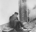 An elderly Jew sitting at an entrance to a house.