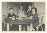 A mother, her two children and a friend sit around a round-wooden table.